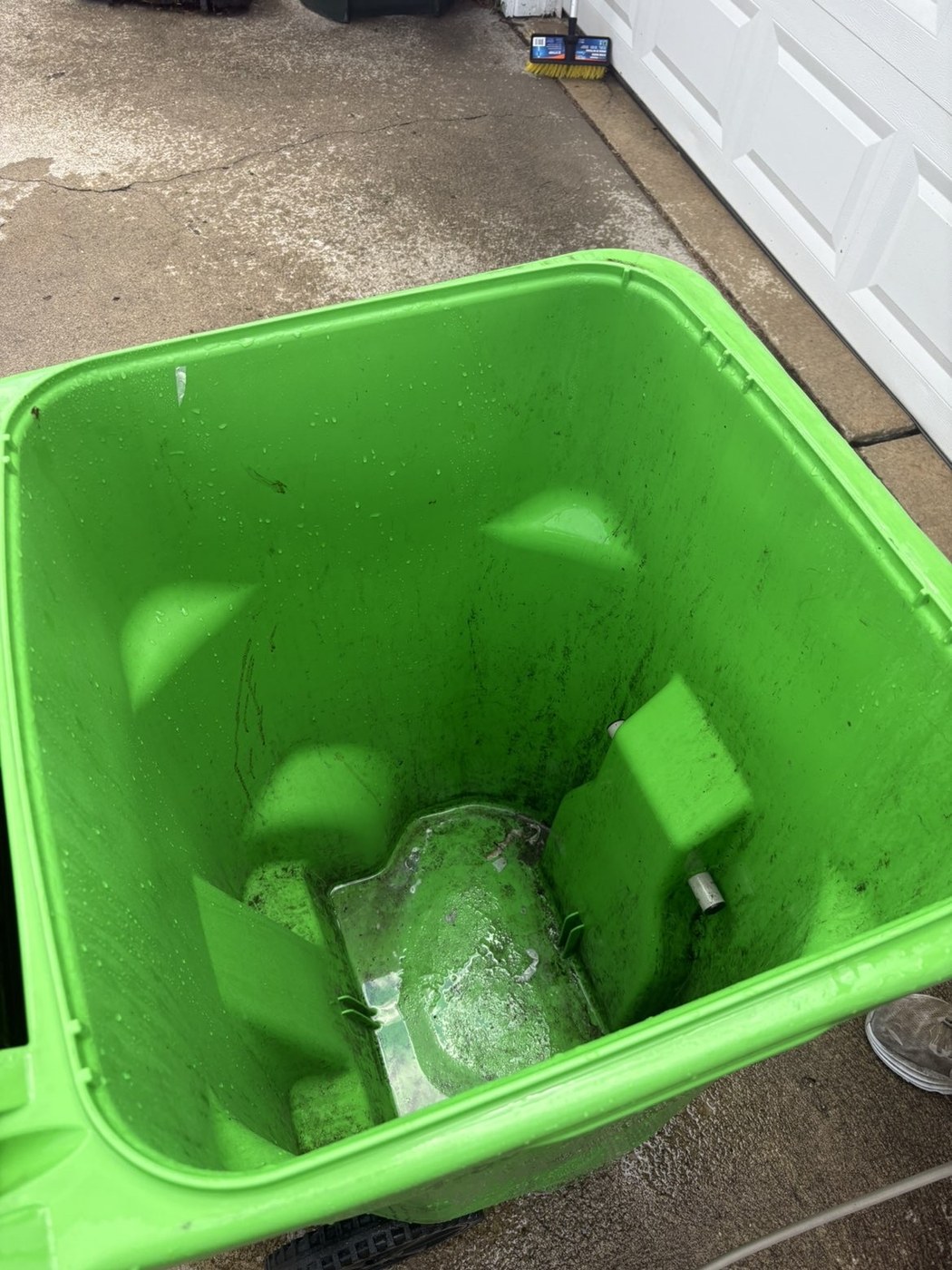 Green trash bin before cleaning with dark buildup inside